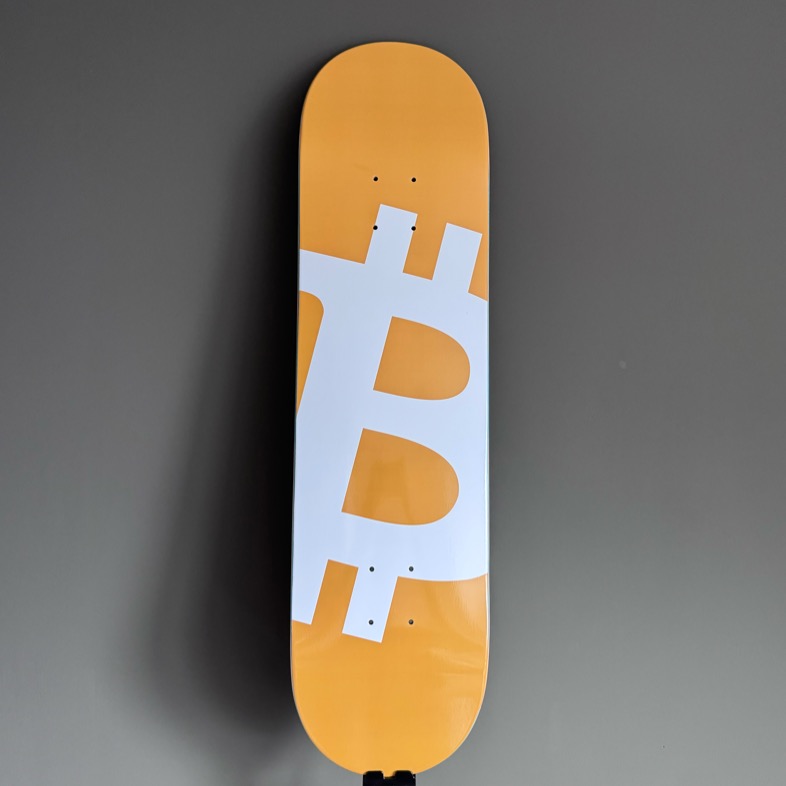 The Genesis — skateboard deck with the Bitcoin symbol in orange and white
